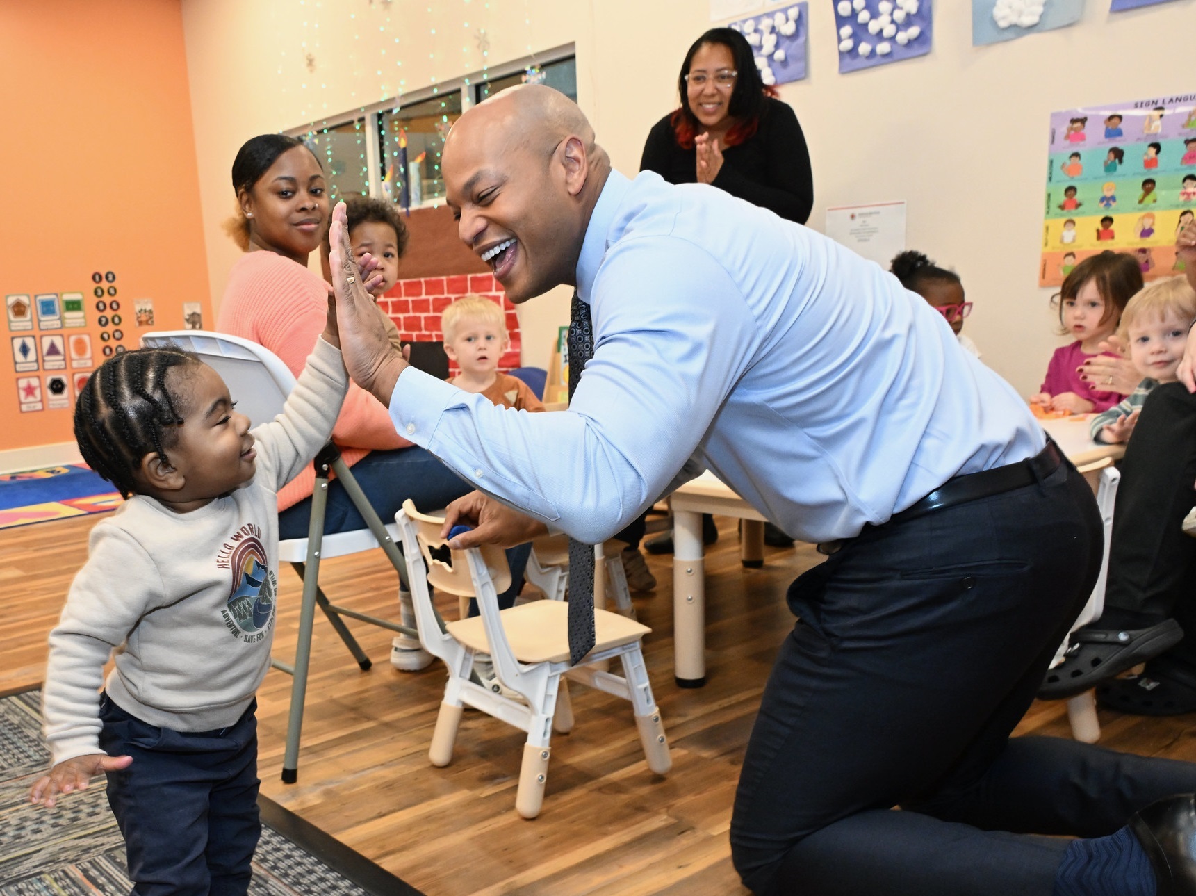 Governor Wes Moore kneels to high-five a toddler inside a colorful child care center.